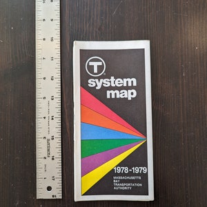 May include: A vintage Massachusetts Bay Transportation Authority system map from 1978-1979. The cover is black with a colorful geometric design and the text "system map". A metal ruler is next to the map, showing measurements in inches.
