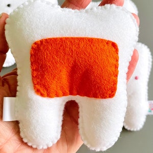 May include: White felt tooth with a bright orange felt patch on the front. The tooth is a plush toy.