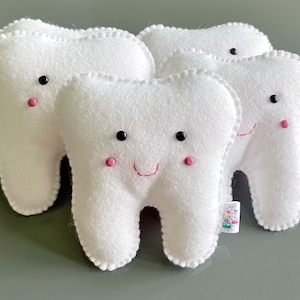 May include: Three white plush teeth with embroidered eyes and pink cheeks. The middle tooth has a red stitched smile.