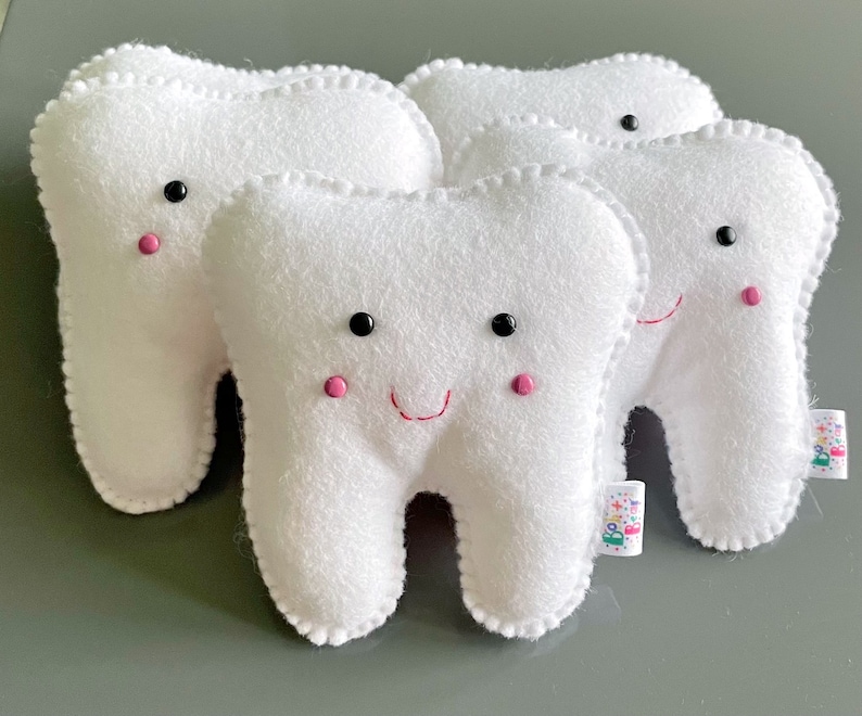 May include: Three white plush teeth with embroidered eyes and pink cheeks. The middle tooth has a red stitched smile.