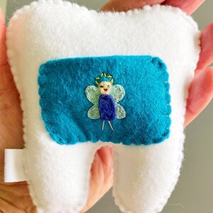 May include: A white felt tooth with a blue felt pocket containing a felt fairy with a yellow crown and green wings.
