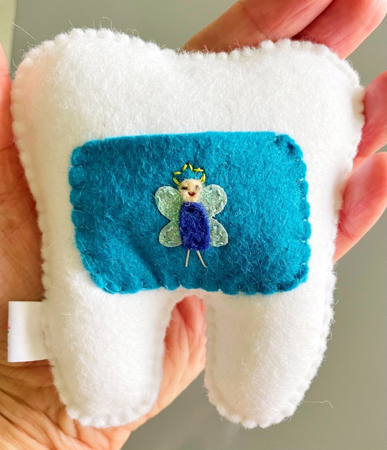 May include: A white felt tooth with a blue felt pocket containing a felt fairy with a yellow crown and green wings.