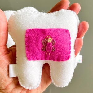 May include: White felt tooth pillow with a pink felt pocket and a sparkly pink butterfly with a gold fairy inside.