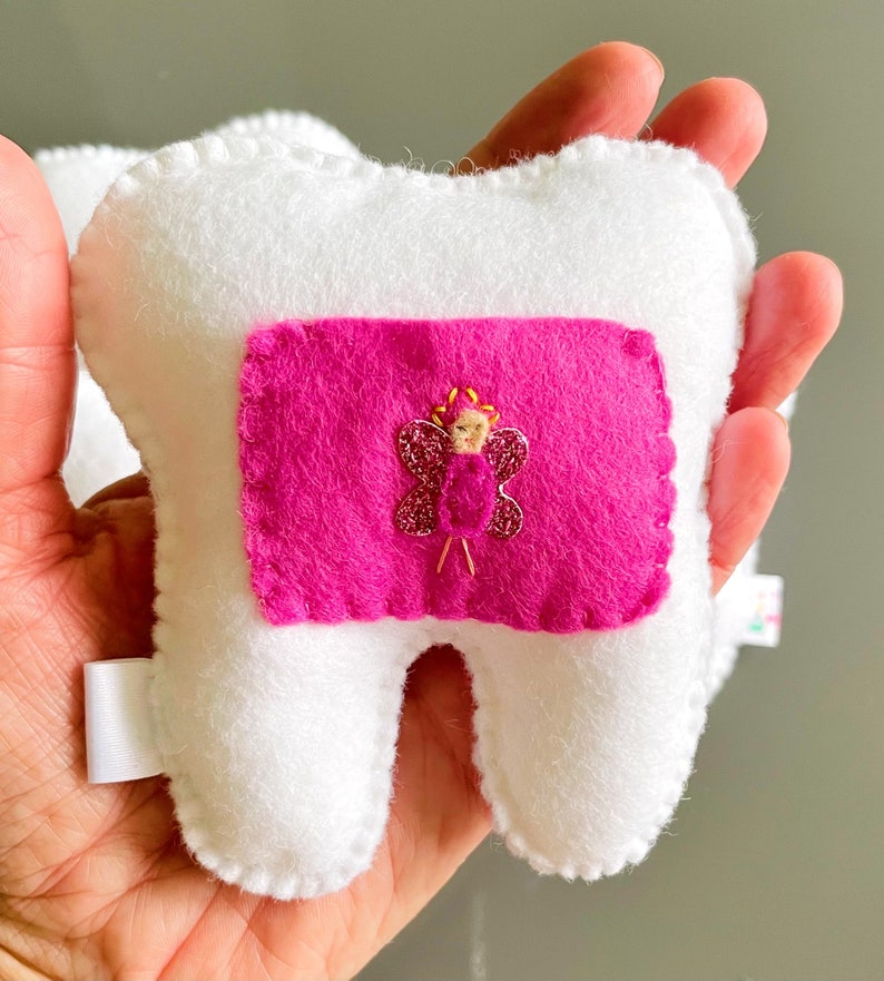 May include: White felt tooth pillow with a pink felt pocket and a sparkly pink butterfly with a gold fairy inside.