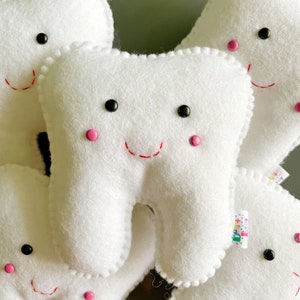 May include: A group of five white felt tooth-shaped plush toys with embroidered smiling faces, black eyes, and pink cheeks.