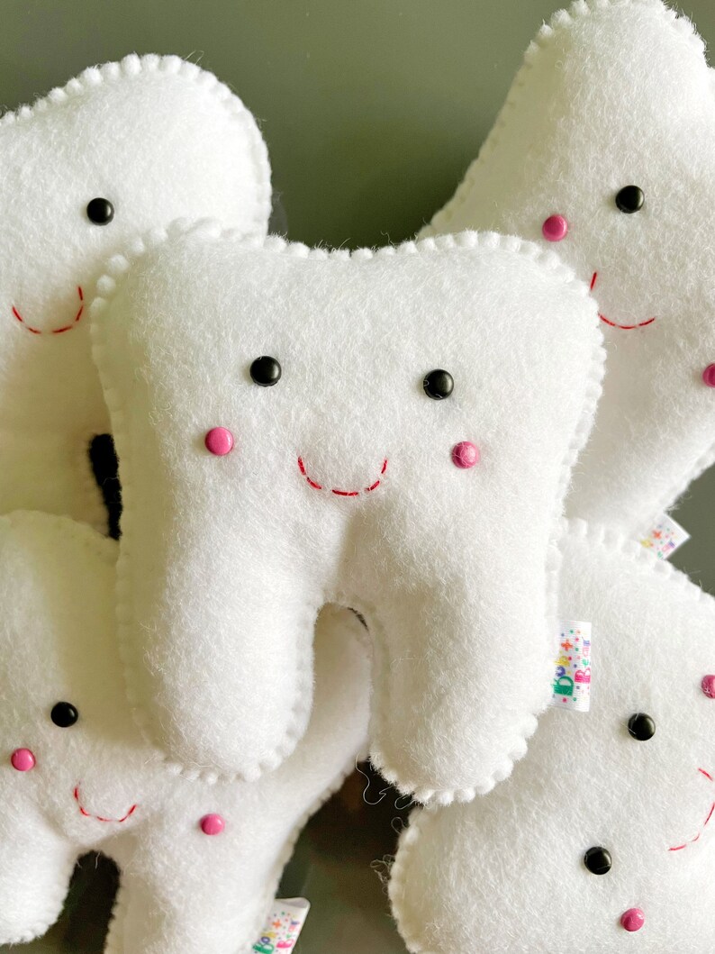 May include: A group of five white felt tooth-shaped plush toys with embroidered smiling faces, black eyes, and pink cheeks.