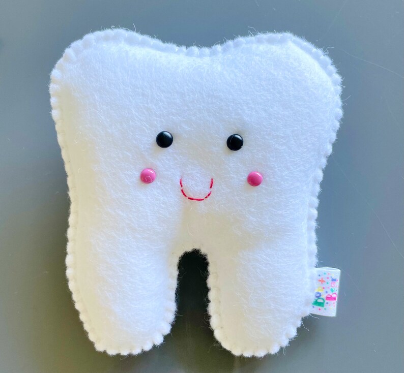 May include: White plush tooth with a smiling face. The tooth has black eyes, pink cheeks, and a red stitched smile.