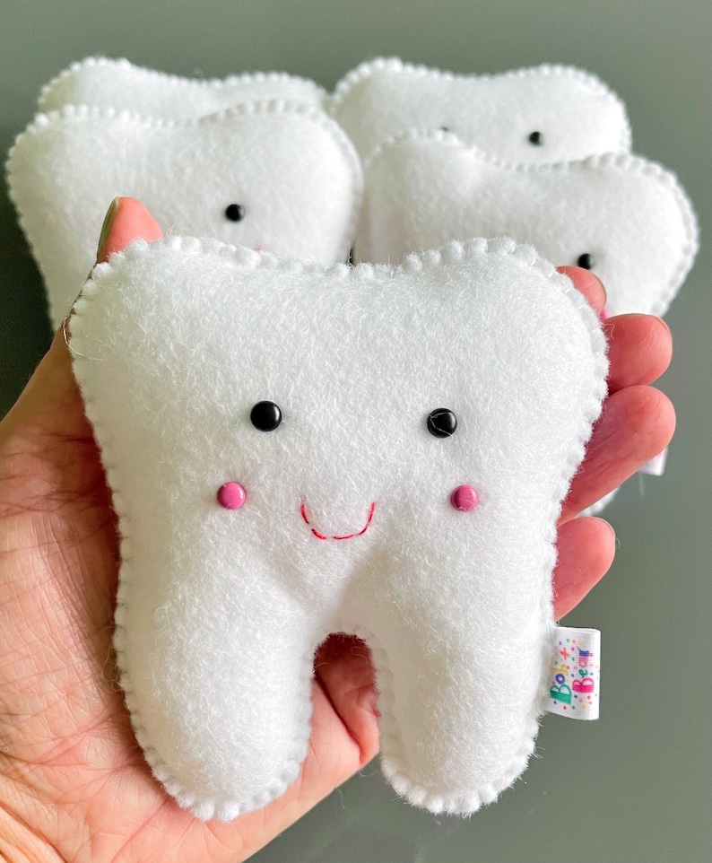 May include: Five white plush teeth with embroidered eyes and pink cheeks. One tooth has a red stitched smile and a small tag that says "Boo Bear".