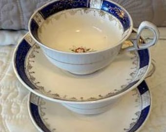 May include: A set of two vintage teacups and saucers with a white background and blue and gold trim. The cups have a floral design in the center.