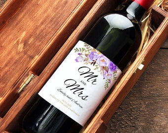 Può includere: Una bottiglia di vino con un'etichetta personalizzata che dice "Mr and Mrs" con un design floreale e la data "04.12.2012". La bottiglia è in una scatola di legno.
