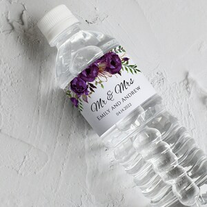 Könnte beinhalten: Eine weiße Wasserflasche mit einem lila floralen Hochzeitsetikett, auf dem "Mr. & Mrs. Emily und Andrew 04.14.2022" steht.