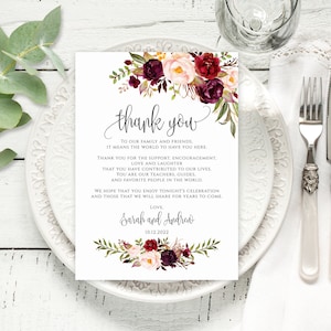 Könnte beinhalten: Eine Dankeskarte mit einem floralen Design in den Farben Burgunderrot, Rosa und Grün. Die Karte trägt die Aufschrift "Danke" in einer kursiv geschriebenen Schrift und enthält den Text "An unsere Familie und Freunde, es bedeutet uns die Welt, euch hier zu haben. Vielen Dank für eure Unterstützung, Ermutigung, Liebe und das Lachen, das ihr in unser Leben gebracht habt. Ihr seid unsere Lehrer, unsere Führer und die Menschen, die wir am meisten auf der Welt lieben. Wir hoffen, dass ihr die heutige Feier genießt und die Momente, die wir in den kommenden Jahren teilen werden. Mit Liebe, Sarah und Andrea, 10.12.2022."