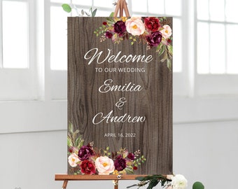 Könnte beinhalten: Rustikales hölzernes Hochzeitsschild mit burgunderrotem und blushfarbenem Blumendesign. Das Schild lautet "Willkommen zu unserer Hochzeit Emilia & Andrew 16. April 2022".