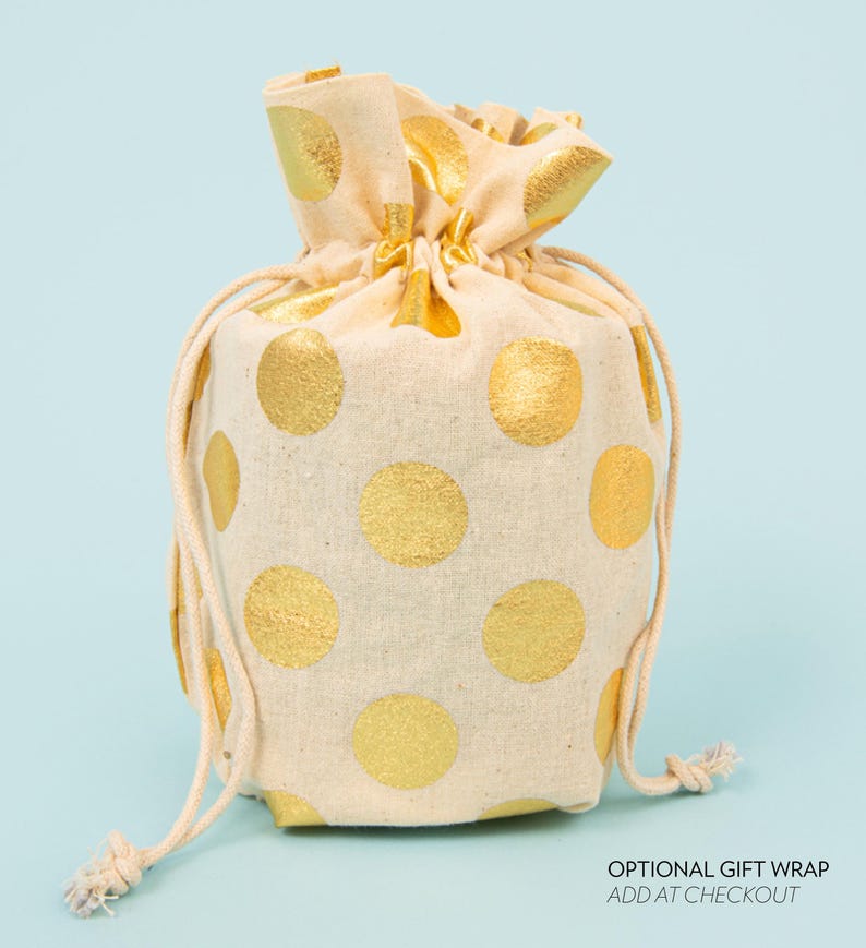 May include: A beige drawstring gift bag with large gold polka dots. The bag is tied at the top with a beige drawstring. The text "OPTIONAL GIFT WRAP ADD AT CHECKOUT" is visible at the bottom right.