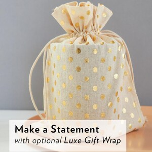 May include: A beige drawstring gift bag with gold polka dots. The bag is tied at the top with a matching drawstring. The text "Make a Statement" is displayed on the bottom of the image.