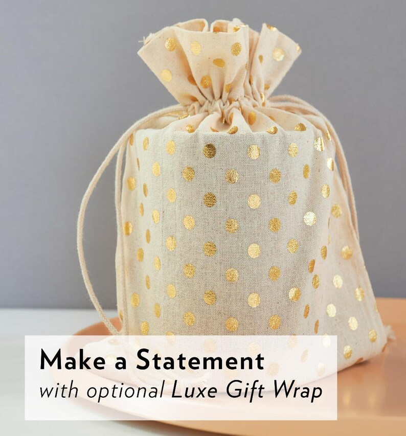 May include: A beige drawstring gift bag with gold polka dots. The bag is tied at the top with a matching drawstring. The text "Make a Statement" is displayed on the bottom of the image.