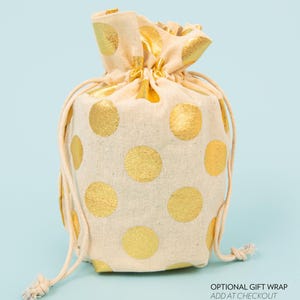 May include: A beige drawstring gift bag with large gold polka dots. The bag is tied at the top with a beige drawstring. The text "OPTIONAL GIFT WRAP ADD AT CHECKOUT" is visible at the bottom right.