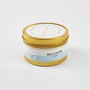 Puede incluir: Vela en lata dorada con una etiqueta blanca que dice "Scripted Fragrance" y "Bulldog candle". La etiqueta tambi&eacute;n presenta una silueta negra de un bulldog.