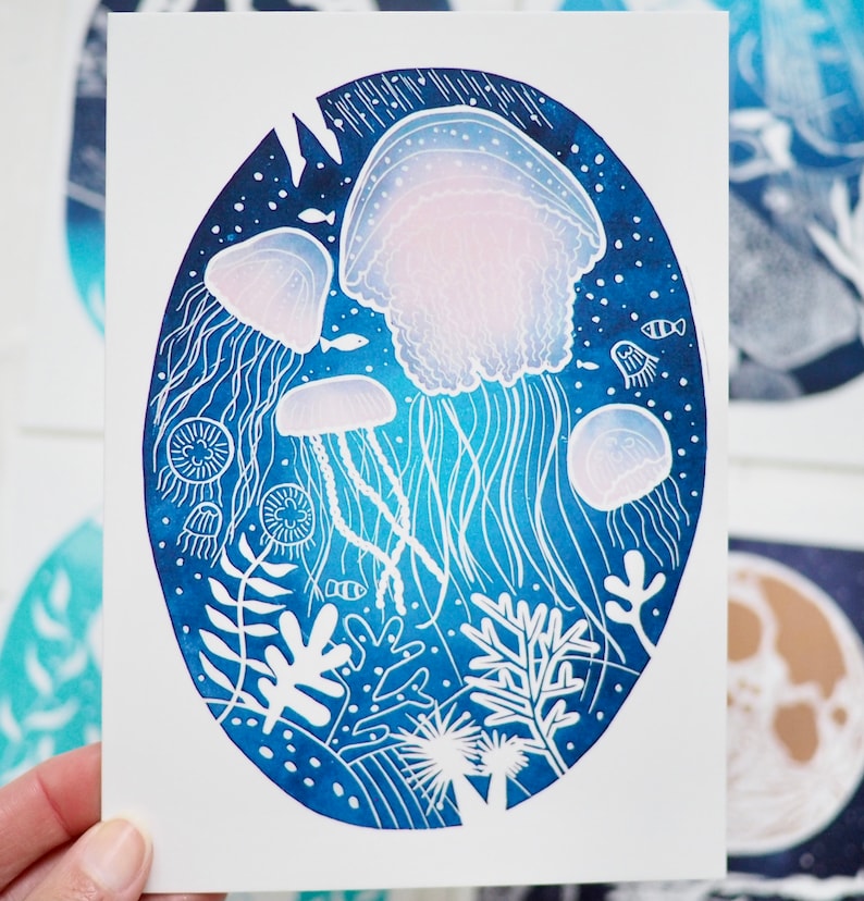 May include: An oval-shaped art print featuring a detailed illustration of jellyfish in a deep blue ocean scene. The jellyfish are white and pink, with long, flowing tentacles. The background includes coral and small fish.