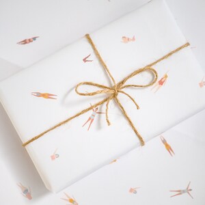 K&ouml;nnte beinhalten: Wei&szlig;es Geschenkpapier mit einer braunen Kordelschleife. Das Papier ist mit einem sich wiederholenden Muster von Schwimmern in verschiedenen Posen verziert.