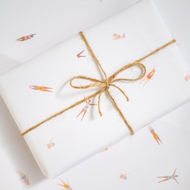 K&ouml;nnte beinhalten: Wei&szlig;es Geschenkpapier mit einer braunen Kordelschleife. Das Papier ist mit einem sich wiederholenden Muster von Schwimmern in verschiedenen Posen verziert.