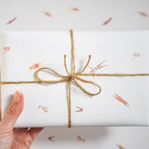 K&ouml;nnte beinhalten: Wei&szlig;es Geschenkpapier mit einer braunen Kordelschleife. Das Geschenkpapier hat ein sich wiederholendes Muster von Schwimmern in verschiedenen Posen.