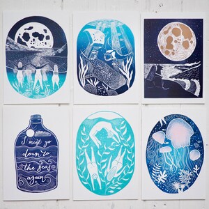 May include: A collection of six art prints featuring ocean-themed illustrations in shades of blue and white. The prints depict scenes such as divers, jellyfish, and a whale shark. One print includes the text "I must go down to the seas again."