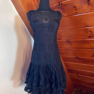 Puede incluir: Una taza de cerámica blanca con un asa negra y el texto "But First, Coffee" en negro, con una fuente de estilo manuscrito. La taza está sobre una superficie blanca.