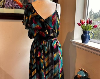 May include: A colorful maxi dress with a V-neck and a chevron pattern in teal, yellow, red, and black. The dress has a ruffled sleeve and a matching belt. The dress is displayed on a mannequin.