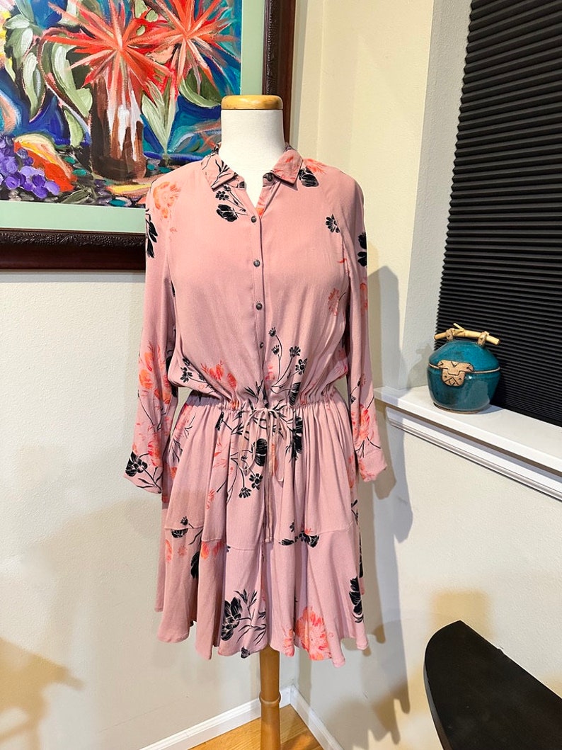 May include: A pink floral dress with long sleeves and a button-up front. The dress has a cinched waist and a tiered skirt.