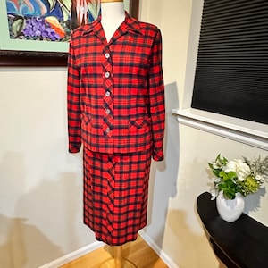 Puede incluir: Un traje de falda rojo y negro a cuadros con una chaqueta abotonada y una falda hasta la rodilla.