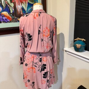 May include: A pink floral dress with black and orange flowers. The dress has long sleeves and a button-up collar.