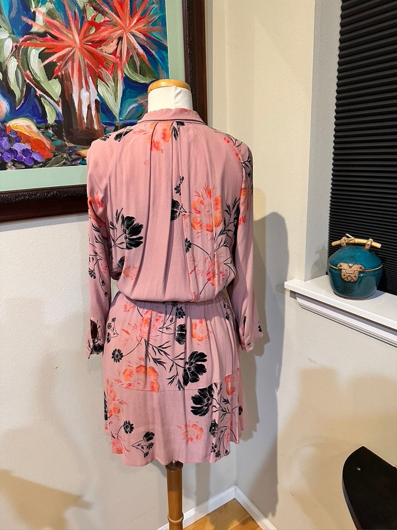 May include: A pink floral dress with black and orange flowers. The dress has long sleeves and a button-up collar.