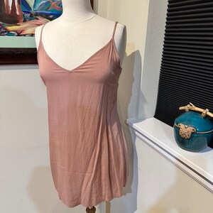 May include: A dusty rose-colored sleeveless slip dress with a V-neckline. The dress is made of a soft, flowing fabric and has a relaxed fit.