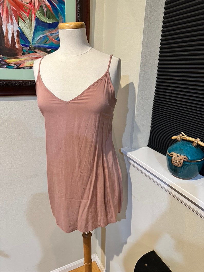 May include: A dusty rose-colored sleeveless slip dress with a V-neckline. The dress is made of a soft, flowing fabric and has a relaxed fit.