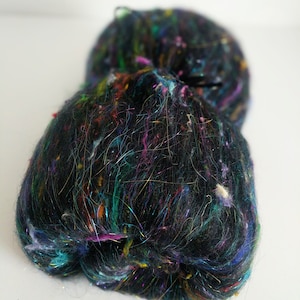 May include: A black yarn with colorful fibers and iridescent threads. The yarn is fluffy and textured.