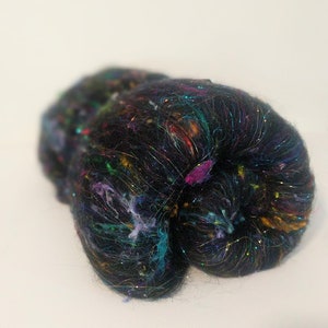May include: A black fiber with iridescent and colorful threads woven throughout. The fiber is loosely packed and has a soft, fluffy texture.