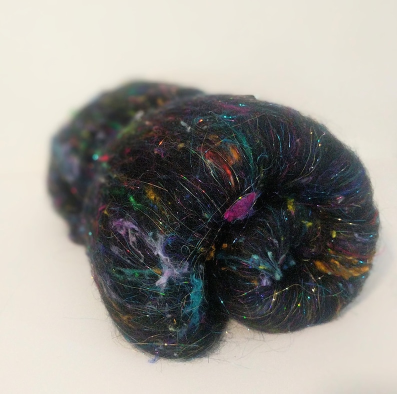 May include: A black fiber with iridescent and colorful threads woven throughout. The fiber is loosely packed and has a soft, fluffy texture.
