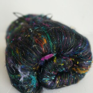 May include: A ball of black yarn with iridescent and colorful fibers. The yarn is made of a blend of fibers, including silk, wool, and metallic threads.