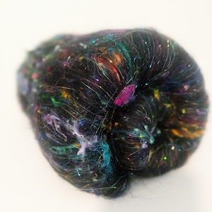 May include: A black fiber with iridescent and colorful fibers woven throughout. The fiber is in a ball shape.