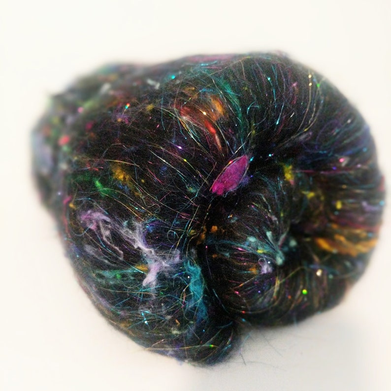 May include: A black fiber with iridescent and colorful fibers woven throughout. The fiber is in a ball shape.
