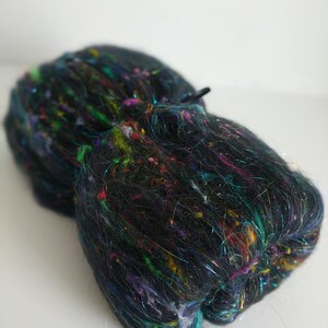 May include: A black fiber with colorful iridescent threads woven throughout. The fiber is bundled and ready for spinning or felting.