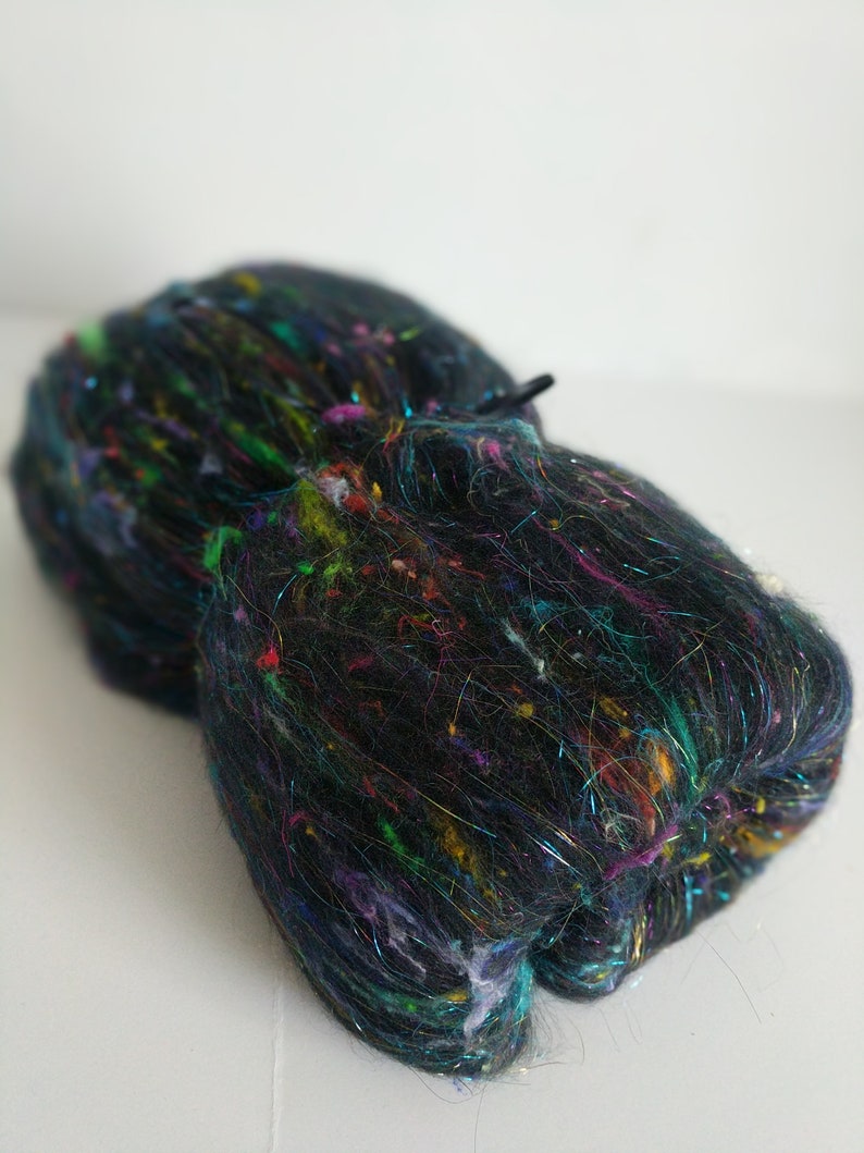 May include: A black fiber with colorful iridescent threads woven throughout. The fiber is bundled and ready for spinning or felting.