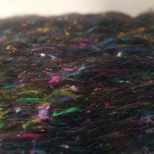 May include: A close-up of a black fabric with a textured surface. The fabric is made of many thin strands of yarn that are woven together. The yarn is a variety of colors, including pink, green, blue, and yellow.