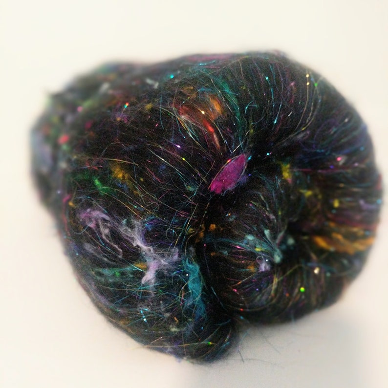 May include: A black fiber with iridescent glitter and colorful fibers throughout. The fiber is loosely packed and appears soft.