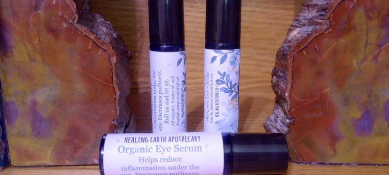 K&ouml;nnte beinhalten: Zwei kleine Glasflaschen mit Roll-on-Applikatoren und wei&szlig;en Etiketten. Die Etiketten tragen den Text "HEALING EARTH APOTHECARY Bio-Augenserum Hilft, Entz&uuml;ndungen unter den Augen zu reduzieren. Reduziert Schwellungen. Aufrollen und einwirken lassen. 100 % nat&uuml;rliches &auml;therisches &Ouml;l"