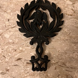 May include: Black cast iron hot pad with a design of a bird in a wreath.