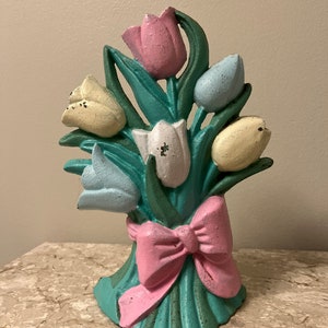 May include: A cast iron doorstop shaped like a bouquet of pastel tulips with a pink bow. The tulips are painted in shades of pink, yellow, and blue.