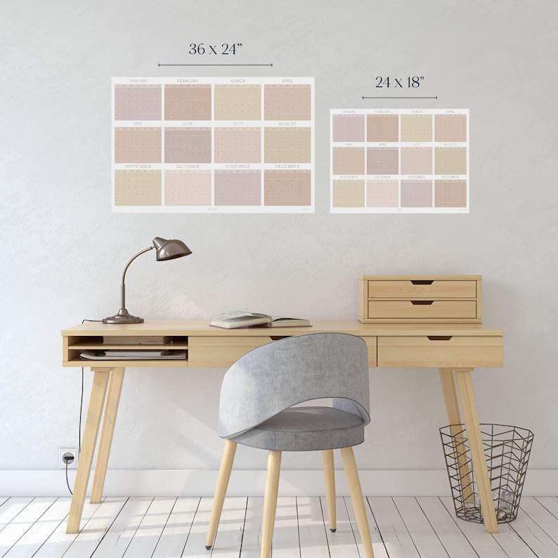 May include: A light wood desk with a lamp, a book, and a wastebasket. A gray chair sits in front of the desk. Two calendars are hanging on the wall behind the desk. The larger calendar is 36 inches by 24 inches and the smaller calendar is 24 inches by 18 inches.