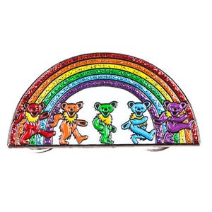 May include: A colorful enamel pin featuring five dancing bears in red, orange, green, blue, and purple, beneath a glittery rainbow. The bears have yellow accents and are set against a white background. This pin is a fun accessory.